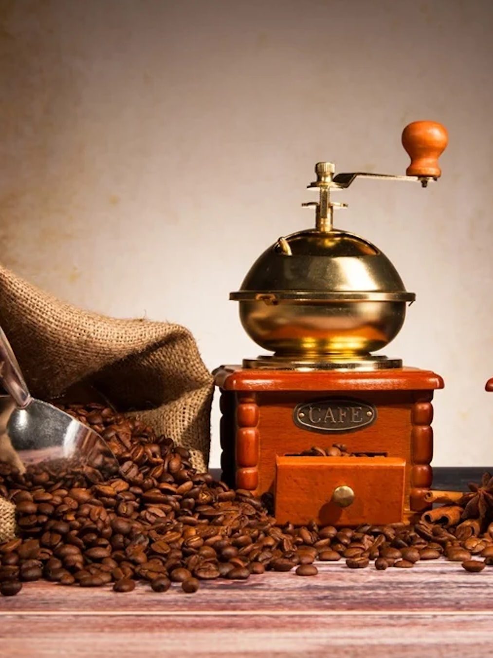Two brass hand grinders beside a burlap sack of roasted beans