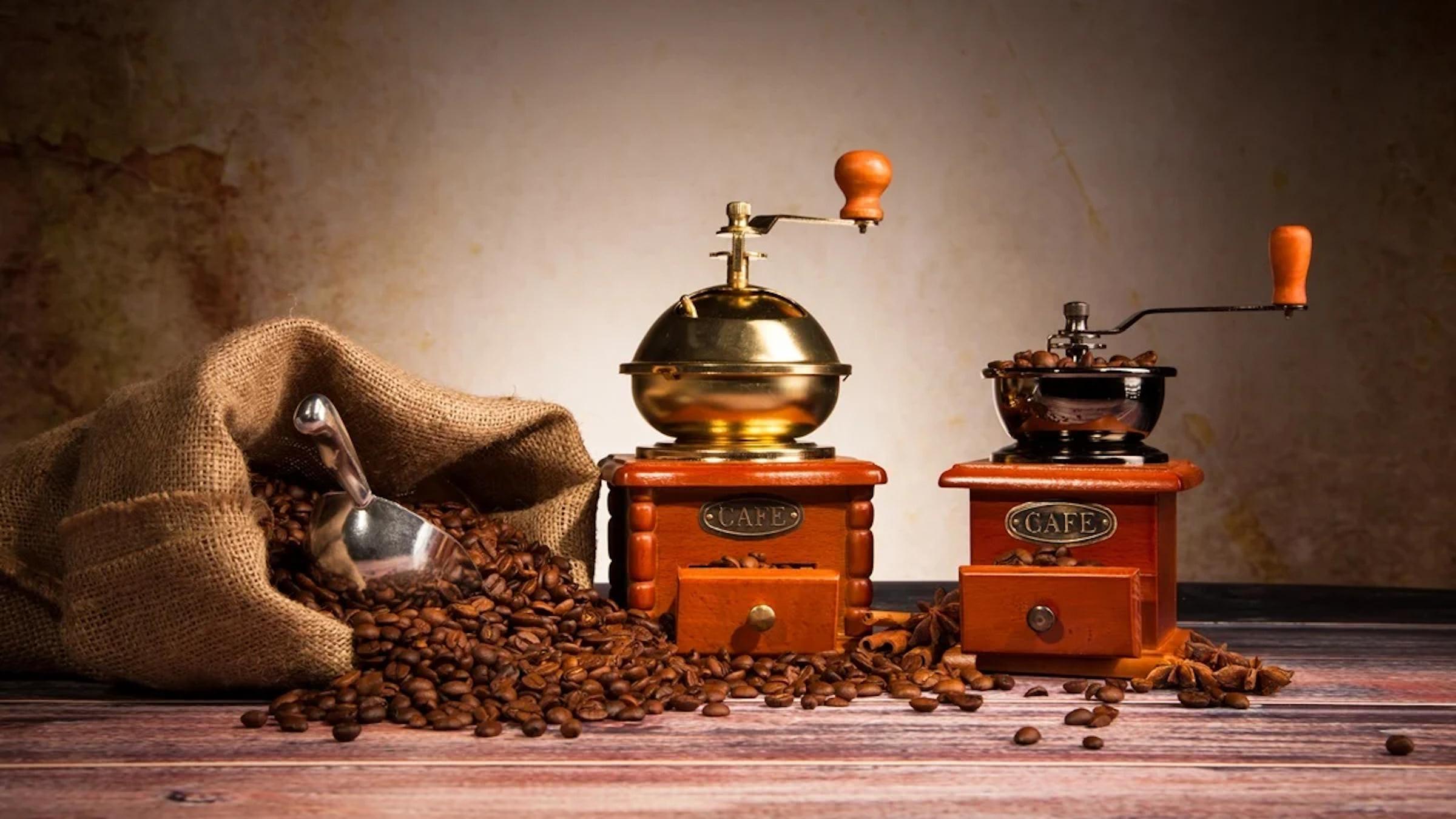 Two brass hand grinders beside a burlap sack of roasted beans